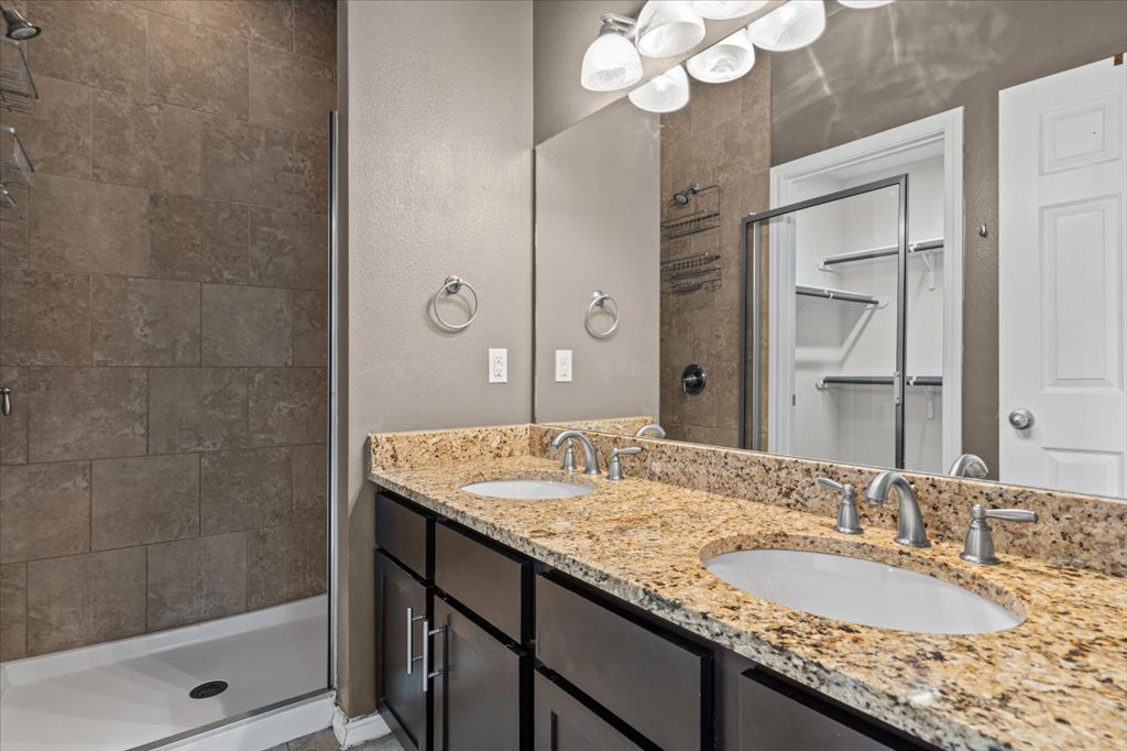 2947 Moss Street Austin, TX 78722 - Photo 12 of 20 Dual vanity with granite countertop and integrated sinks, contemporary light fixture, large mirror, and tiled walk-in shower with glass enclosure