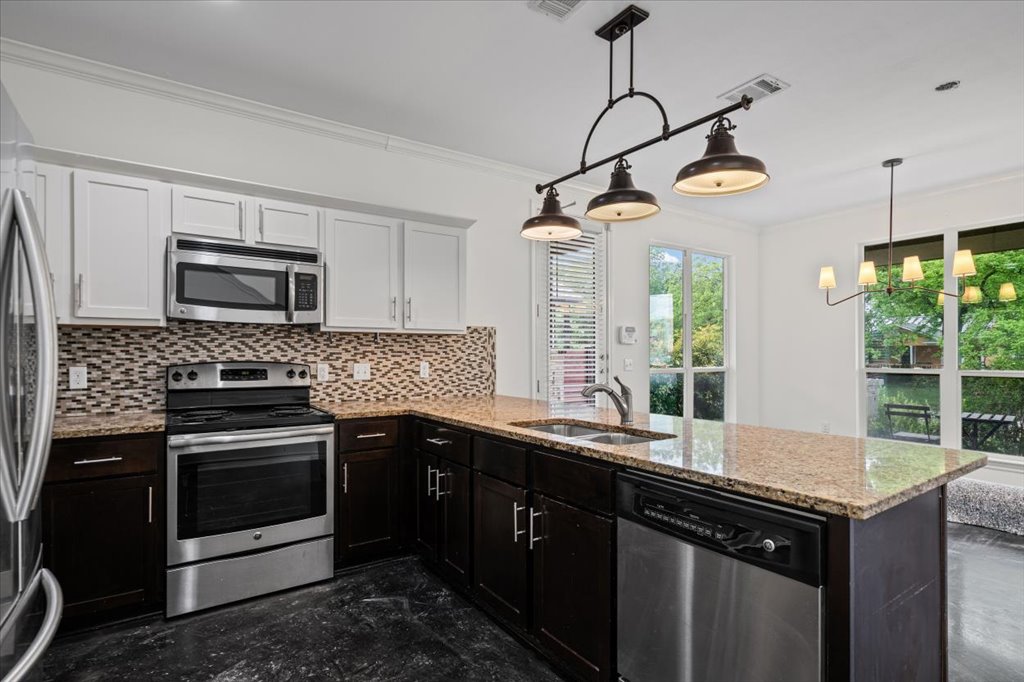 2947 Moss Street Austin, TX 78722 - Photo 7 of 20 Modern kitchen featuring a two-toned cabinetry scheme with white upper cabinets and dark wood-finish lower cabinets, granite countertops, a mosaic tile backsplash, and stainless steel appliances including a range, microwave, and dishwasher