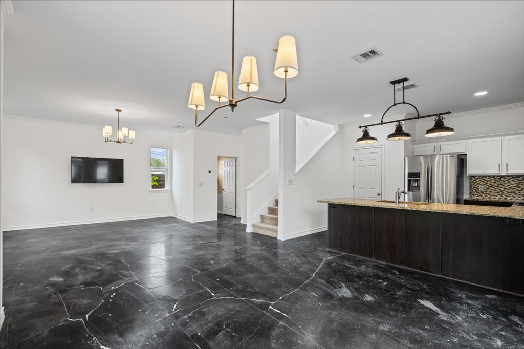2947 Moss Street Austin, TX 78722 - Photo 8 of 20 Open-concept living area featuring dark marbled flooring, a modern linear chandelier, and a kitchen island with stone countertops and a dark wood-finish base