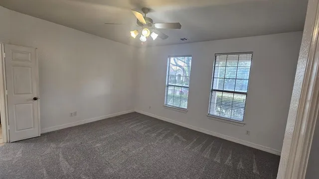 an empty room with chandelier fan and windows