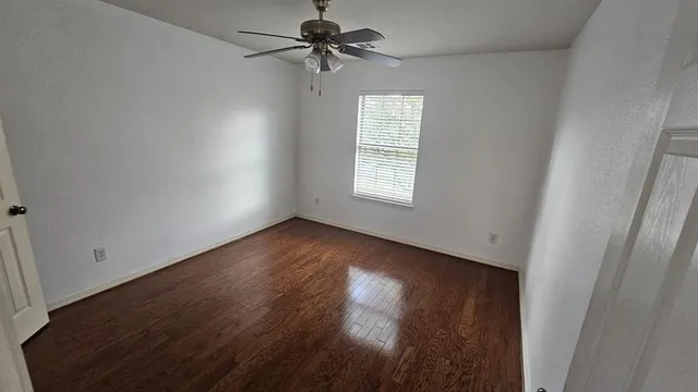 an empty room with wooden floor fan and windows