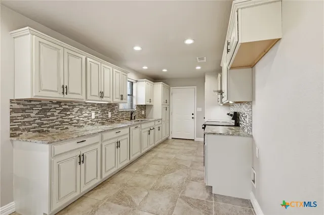 a kitchen with stainless steel appliances granite countertop a stove a sink and white cabinets