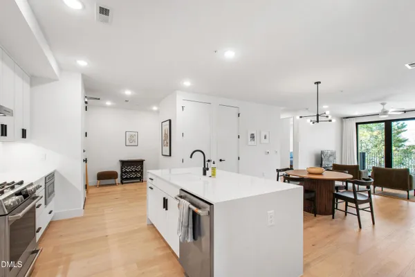 a large white dining hall with stainless steel appliances kitchen island a stove a sink a dining table and chairs