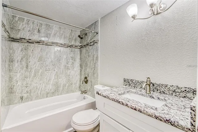 a bathroom with a granite countertop bathtub shower sink vanity and toilet