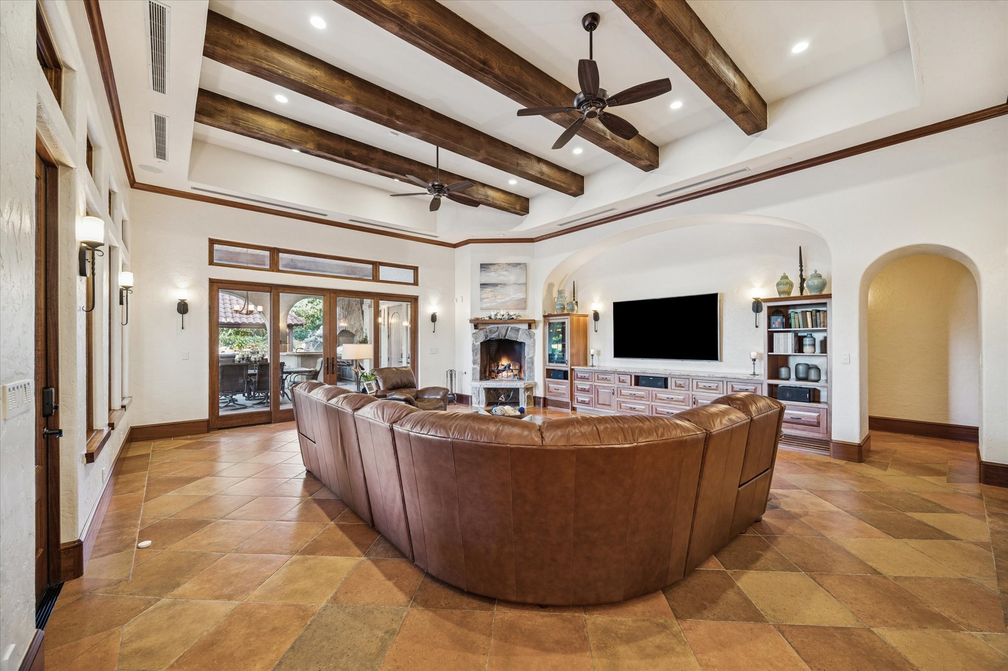 21538 Mueschke Road Tomball, TX 77377 - Photo 16 of 50 Open-concept family room. Connecting seamlessly to the kitchen and breakfast area, this space is perfect for family gatherings and game nights. The oversized natural stone wood-burning fireplace creates a cozy ambiance, ideal for roasting marshmallows on chilly evenings. Built-in cabinets provide storage, while wood-beam ceilings, crown moldings, Saltillo tile floors, granite countertops, and abundant natural light enhance the warm Hacienda-Mediterranean style with beautiful outdoor views.