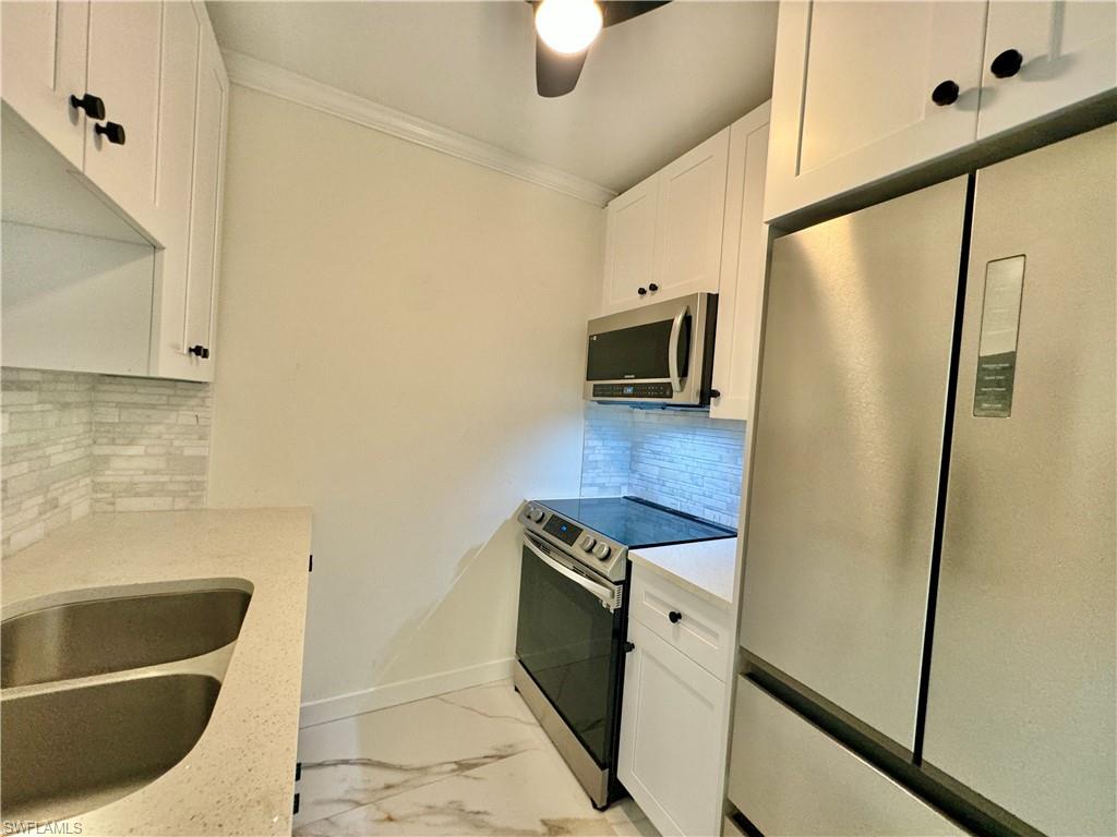 473 12th Avenue South, Unit B7 Naples, FL 34102 - Photo 7 of 21 Kitchen featuring appliances with stainless steel finishes, white cabinetry, backsplash, and ceiling fan