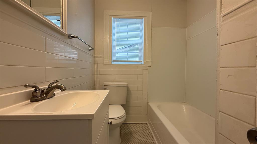 2246 Anson Road Dallas, TX 75235 - Photo 15 of 20 Bathroom featuring a white vanity with integrated sink, chrome faucet, subway tile wainscoting, and a white tub with panel surround