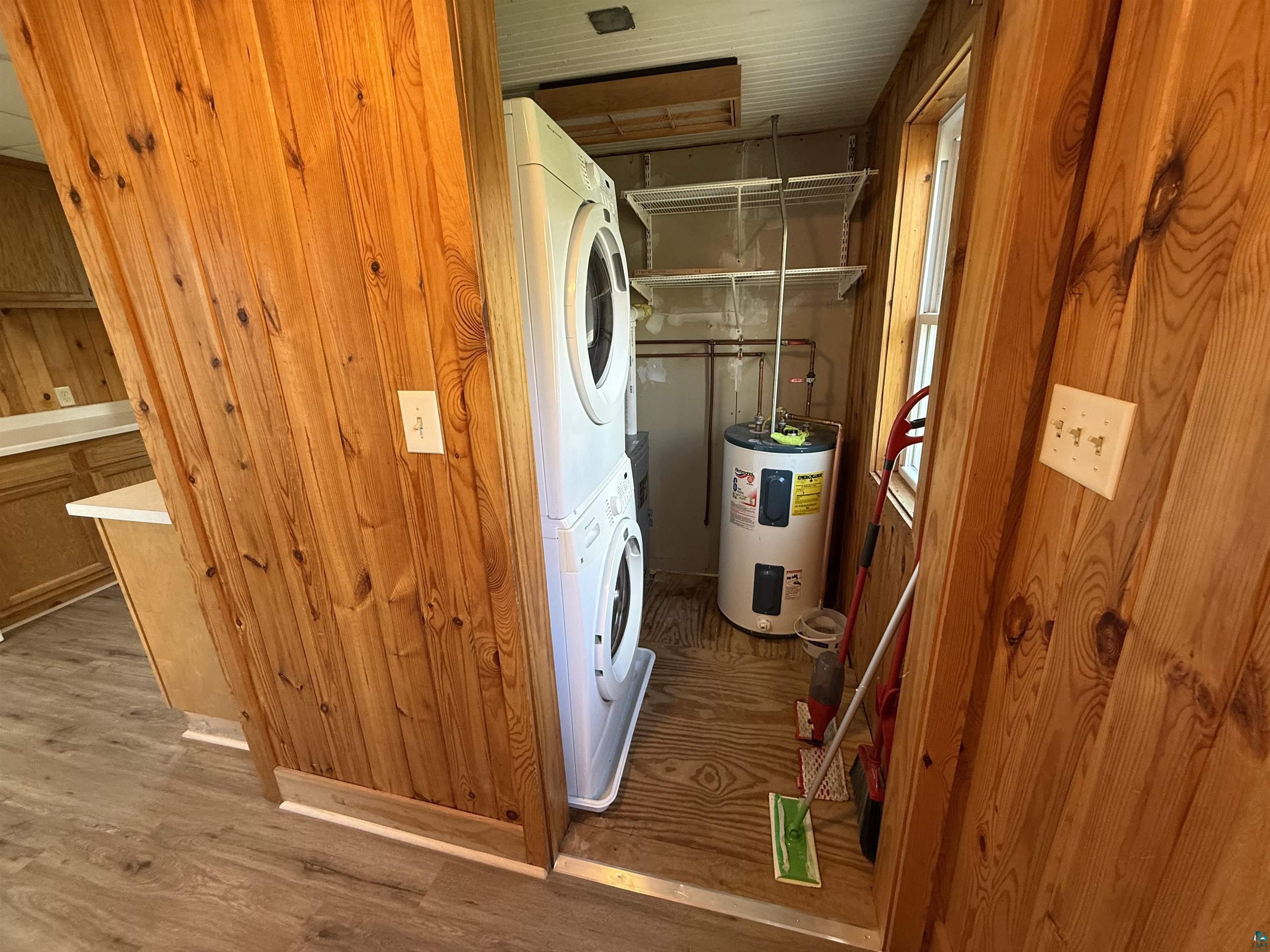 3841 Haines Road Hermantown, MN 55811 - Photo 9 of 11 Dedicated utility area featuring a stacked washer and dryer, wood-finish flooring, paneled walls, a window, and shelving