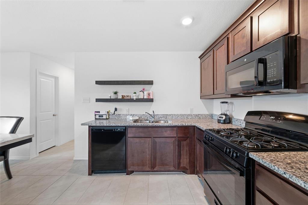 421 Corsair Way Ferris, TX 75125 - Photo 5 of 34 Kitchen with black appliances, light stone countertops, dark wood finish cabinetry, and open shelves