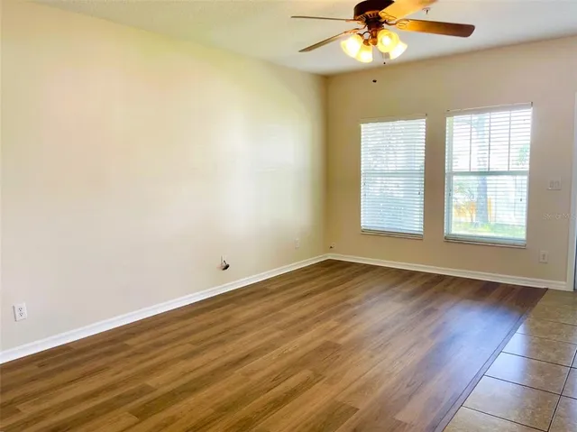 an empty room with wooden floor fan and windows