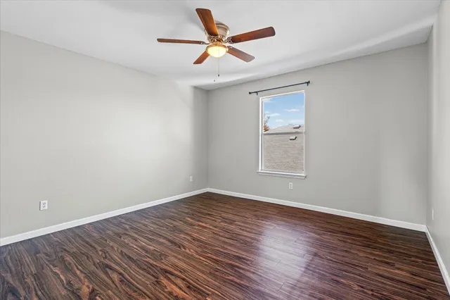 a view of an empty room with wooden floor and a ceiling fan