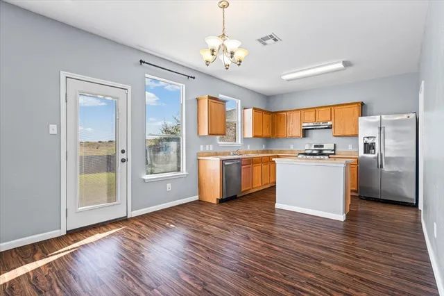 a kitchen with stainless steel appliances granite countertop a refrigerator a sink dishwasher a stove and white countertops with wooden floor