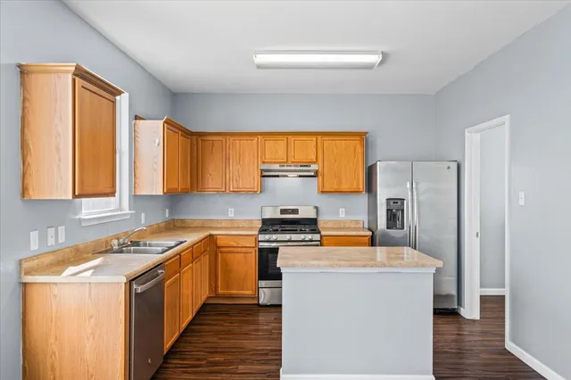 a kitchen with stainless steel appliances a stove a refrigerator a sink dishwasher and wooden cabinets with wooden floor