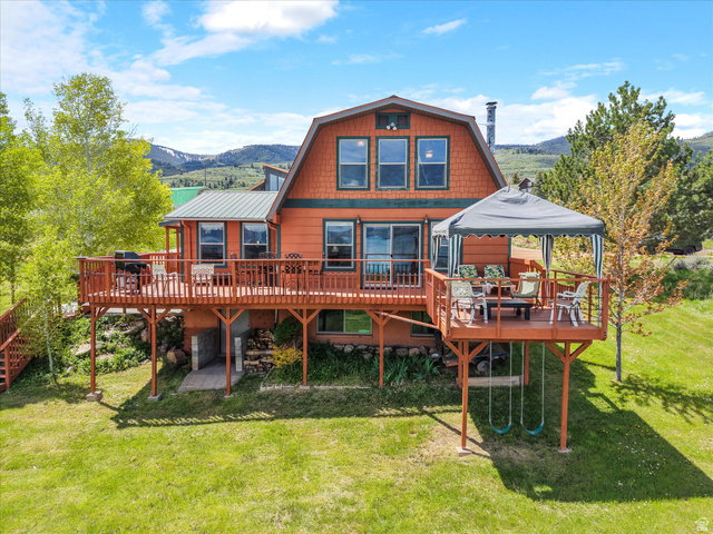Gambrel-style home featuring an expansive wood deck, multiple large windows, and a covered outdoor dining area