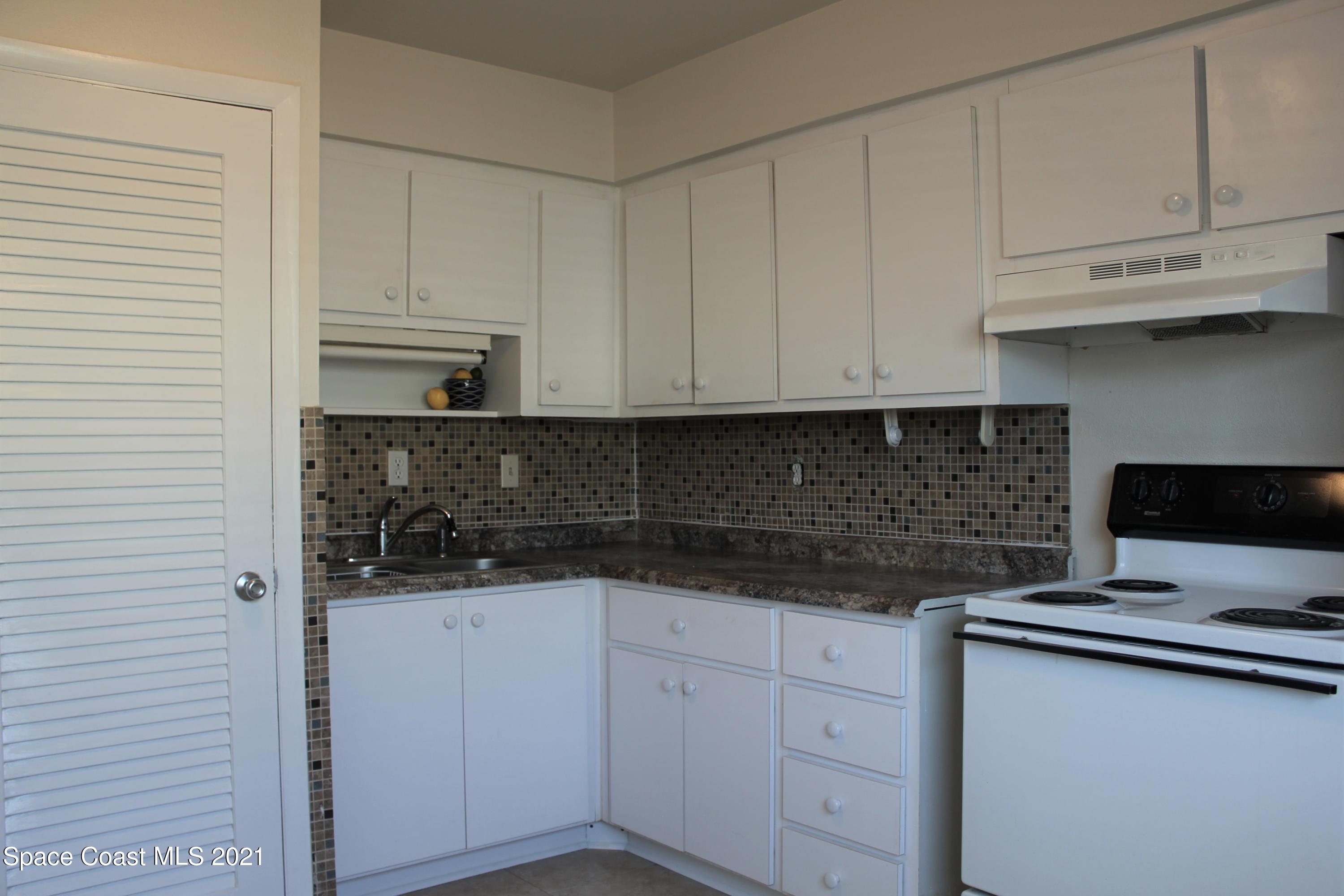 651 Palm Drive, Unit E1 Satellite Beach, FL 32937 - Photo 11 of 18 a kitchen with stainless steel appliances granite countertop white cabinets sink and a granite counter top