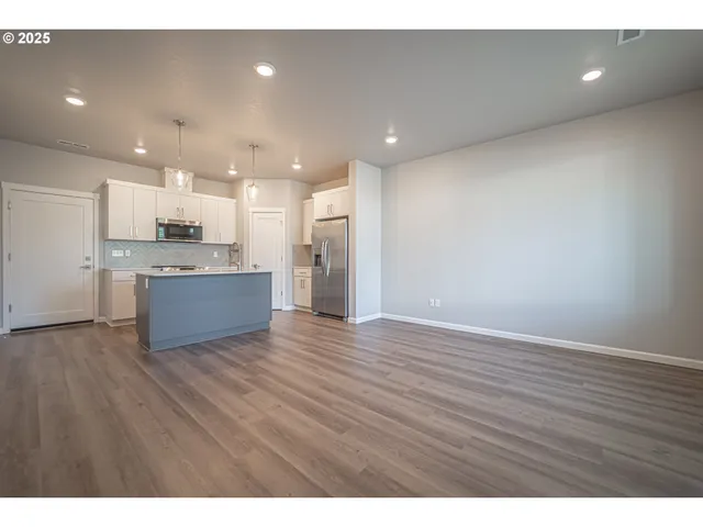 a view of an empty room and kitchen with wooden floor