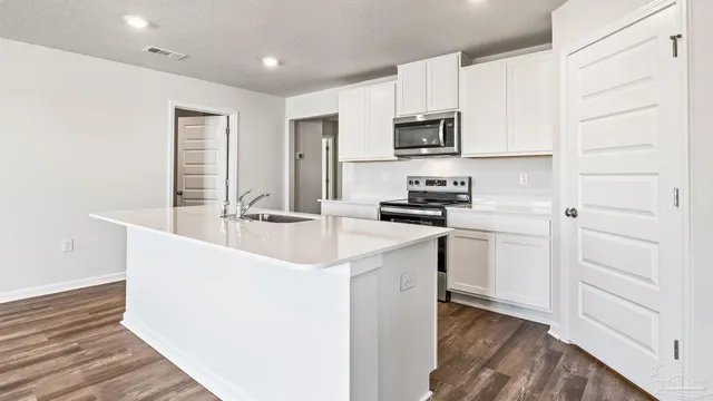 a kitchen with stainless steel appliances a sink dishwasher a stove and white cabinets with wooden floor