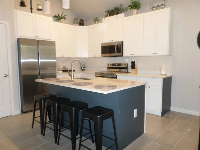 a kitchen with stainless steel appliances a sink a stove a refrigerator with white cabinets and wooden floor