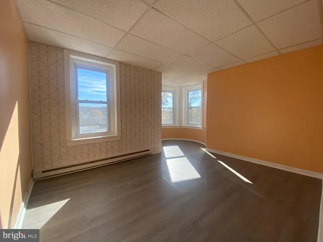 an empty room with wooden floor and windows with curtains