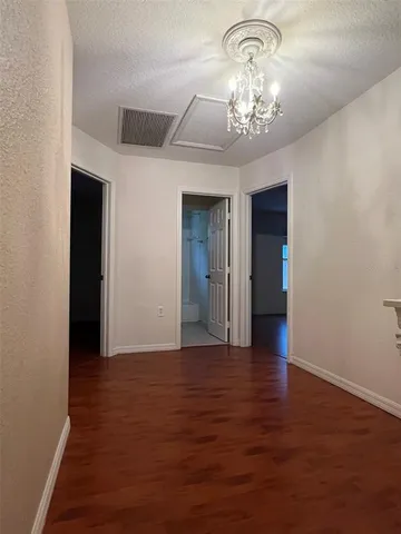 an empty room with wooden floor chandelier and entryway