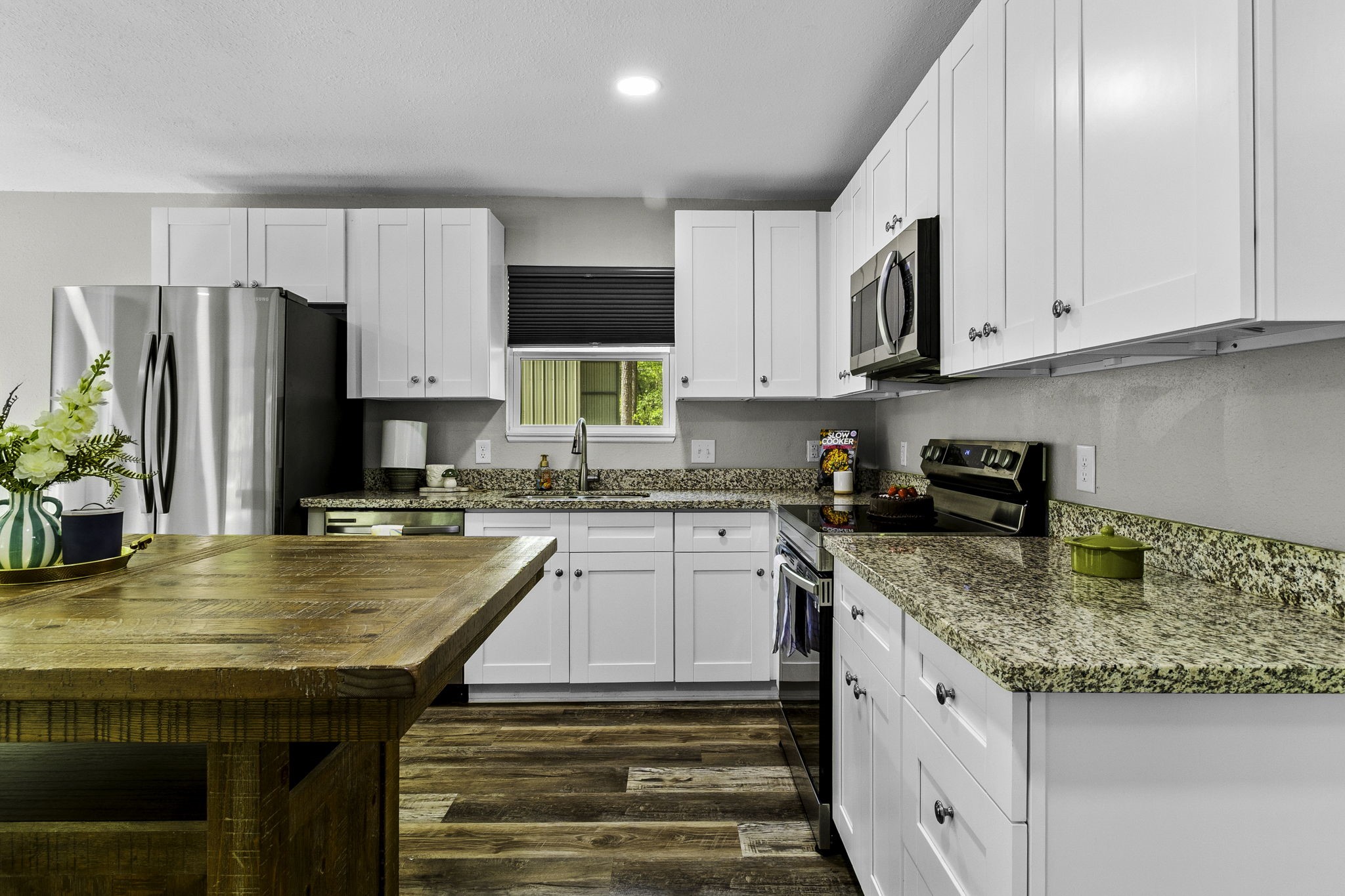 21 Red Oak Circle Point Blank, TX 77364 - Photo 9 of 32 This kitchen features modern white cabinetry, granite countertops, and stainless steel appliances. A spacious wooden island offers additional workspace, complemented by warm wood flooring and ample natural light.
