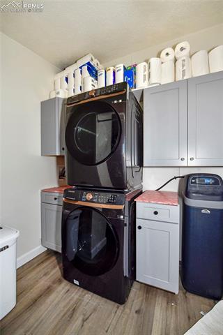 20480 Enoch Road Colorado Springs, CO 80928 - Photo 32 of 45 Washroom featuring cabinets, stacked washing maching and dryer, and hardwood / wood-style floors