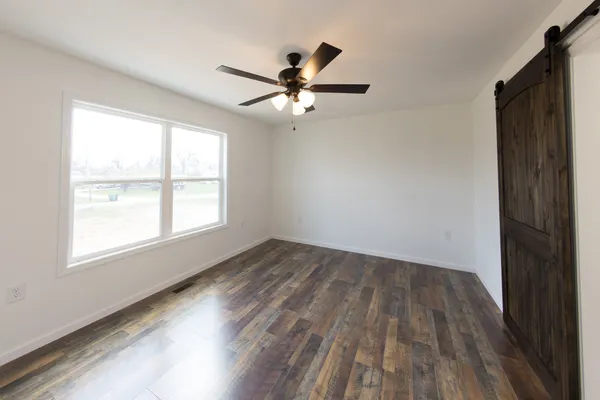 an empty room with wooden floor fan and windows