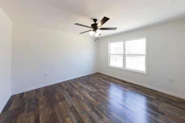 an empty room with wooden floor fan and windows