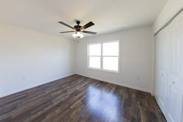 an empty room with wooden floor fan and windows