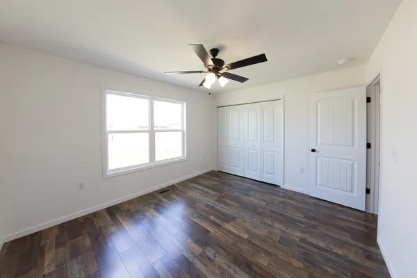 an empty room with wooden floor ceiling fan and windows