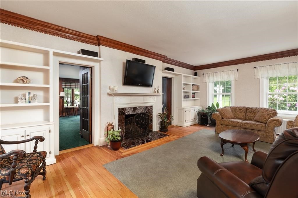 Living room with a high end fireplace, light wood finished floors, built in shelves, and ornamental molding