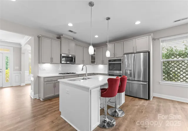 a kitchen with stainless steel appliances granite countertop a refrigerator a stove a sink dishwasher a dining table and chairs with wooden floor