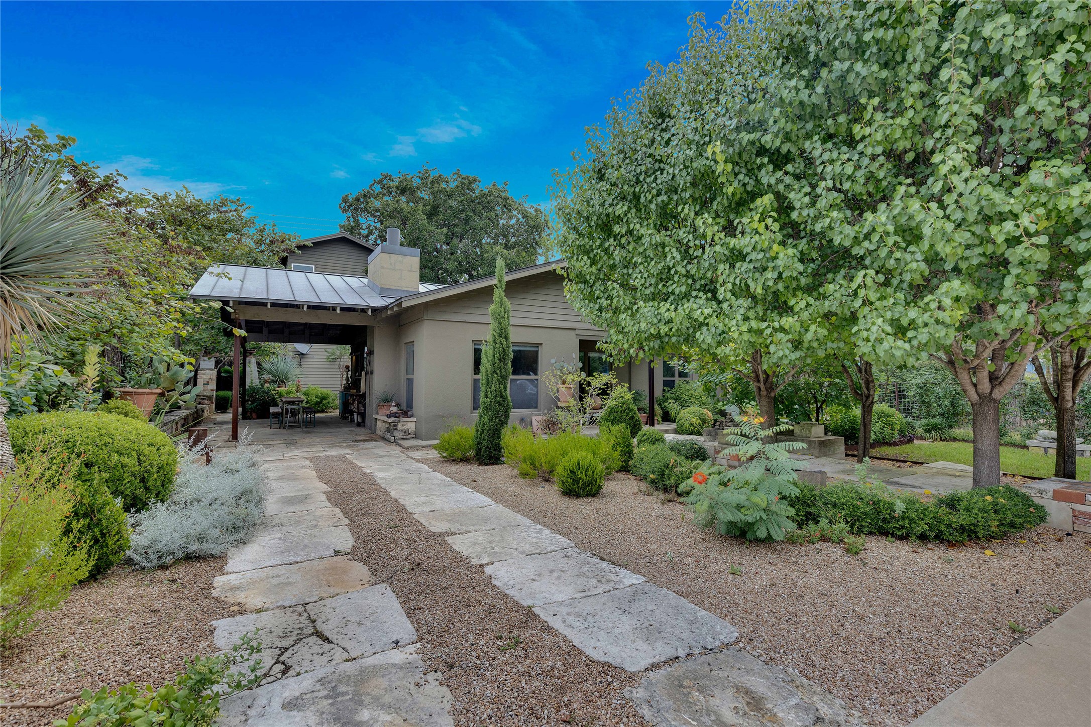 1306 Norwood Road, Unit A Austin, TX 78722 - Photo 1 of 21 Mature trees frame a charming residence with a stone and gravel driveway, offering serene outdoor living.