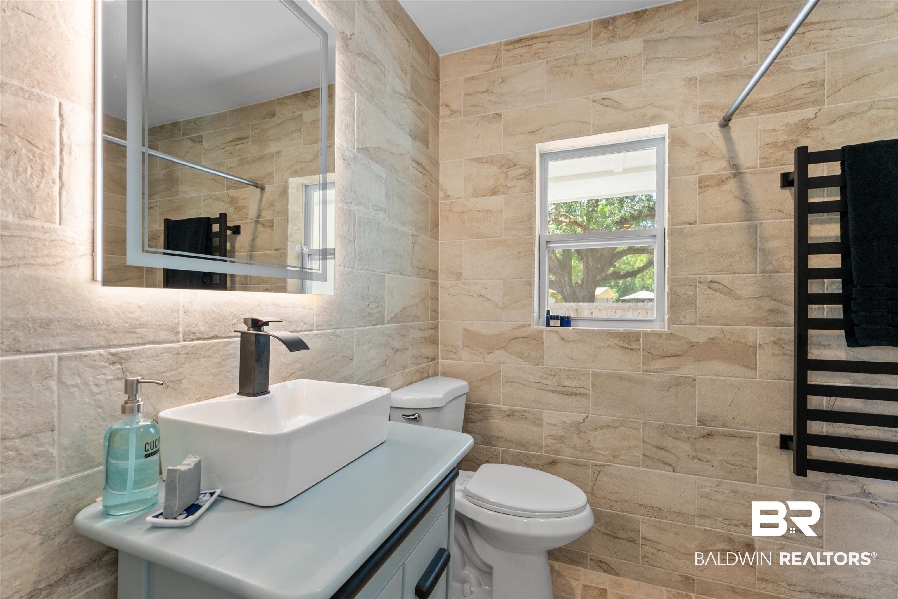 6447 Bemis Lane Bon Secour, AL 36511 - Photo 32 of 62 Modern bathroom featuring a rectangular vessel sink with a dark-finish faucet, a backlit vanity mirror, and a sleek toilet