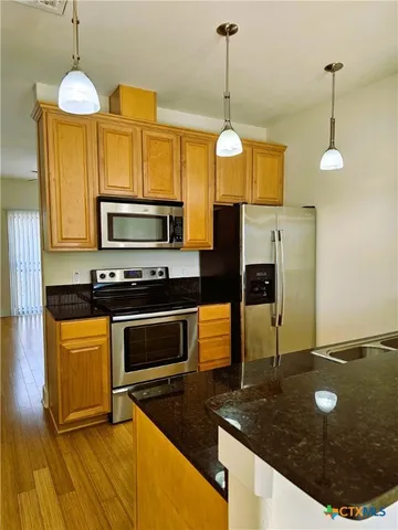 a kitchen with stainless steel appliances granite countertop a stove a sink a refrigerator and a wooden floor
