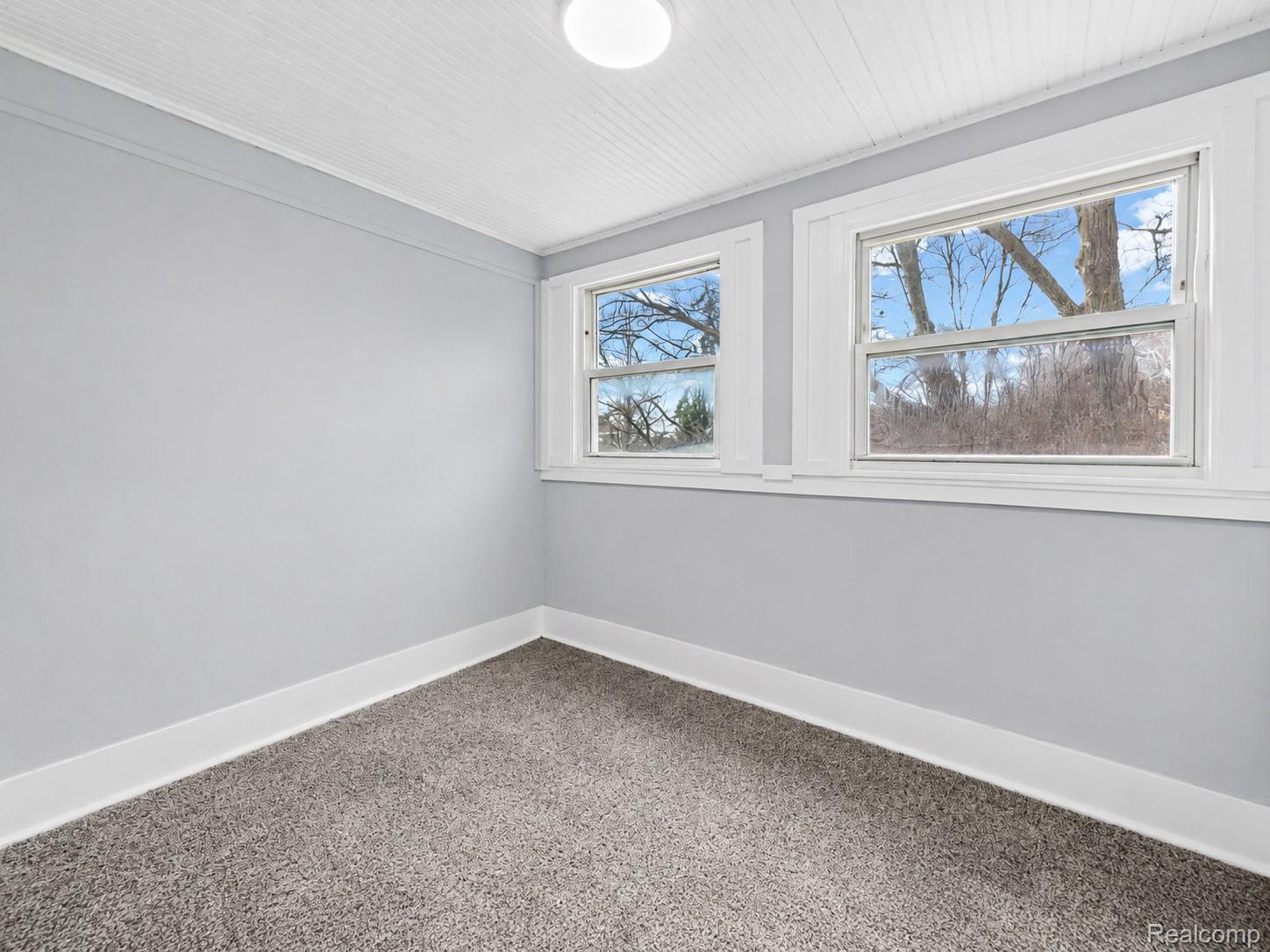 9175 Devonshire Road Detroit, MI 48224 - Photo 19 of 23 Neutral-toned room featuring a light gray carpet, multiple double-hung windows with white trim, and a white beadboard ceiling with a flush-mount light fixture