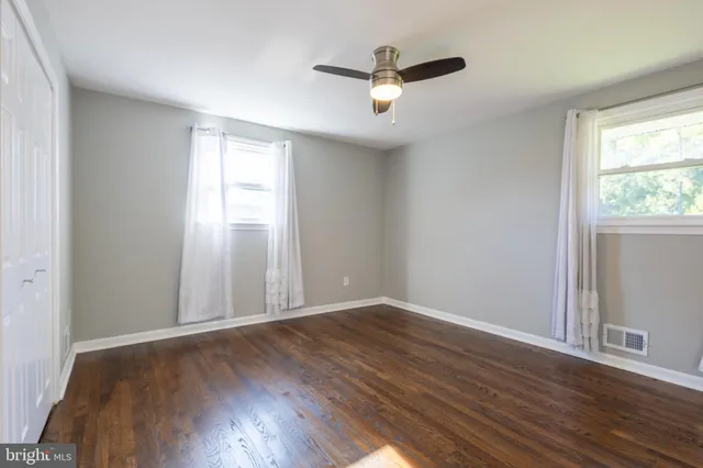 an empty room with wooden floor chandelier fan and windows