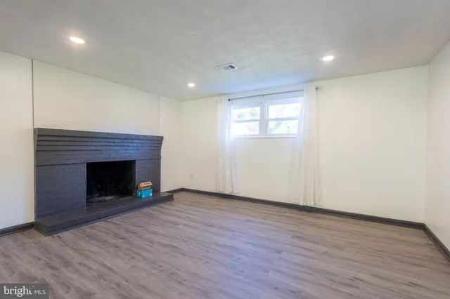 a view of an empty room with wooden floor fireplace and a window