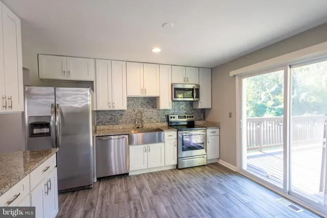 a kitchen with stainless steel appliances granite countertop a refrigerator a stove top oven a sink and dishwasher with wooden floor