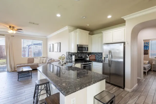 a kitchen with stainless steel appliances granite countertop a refrigerator a stove a sink a dining table and chairs with wooden floor