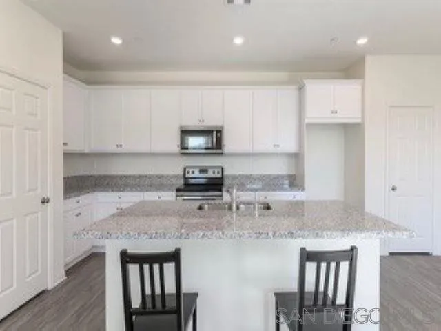 365 Fitzpatrick Road, Unit 102 San Marcos, CA 92069 - Photo 6 of 11 a kitchen with kitchen island granite countertop a stove top oven a sink a counter space and cabinets
