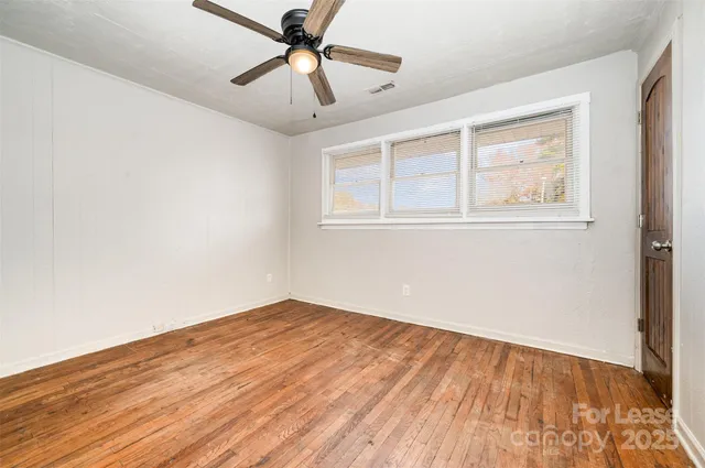 an empty room with wooden floor fan and windows