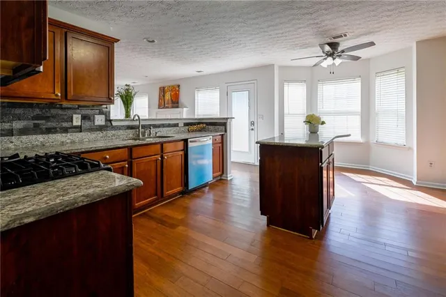 a kitchen with stainless steel appliances granite countertop wooden cabinets a stove top oven a sink and dishwasher with wooden floor