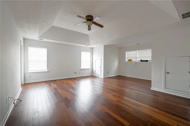 an empty room with wooden floor ceiling fan and windows