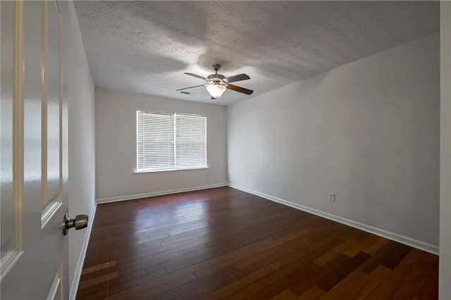 an empty room with wooden floor chandelier fan and windows