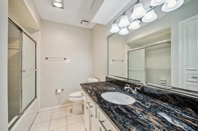 a bathroom with a granite countertop double vanity sink a mirror and a toilet