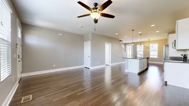 a view of an empty room and kitchen view with wooden floor