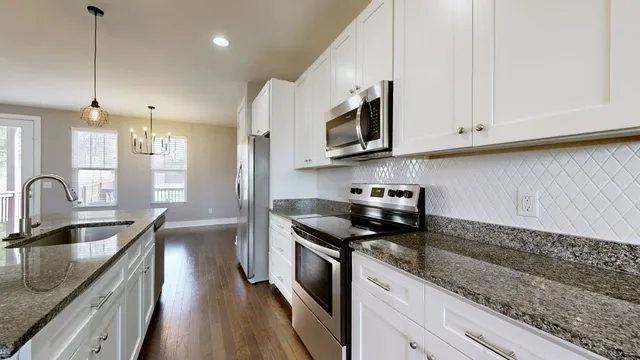 a kitchen with stainless steel appliances granite countertop a sink a stove oven a refrigerator with white cabinets and granite countertops