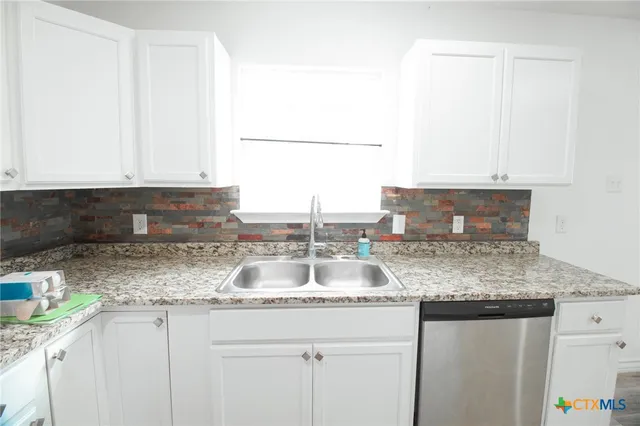 a kitchen with granite countertop a sink and a white cabinets