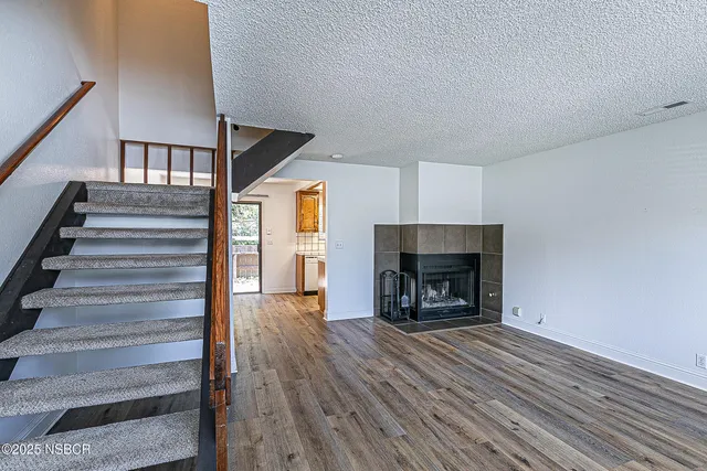 a view of an empty room with wooden floor fireplace and a window